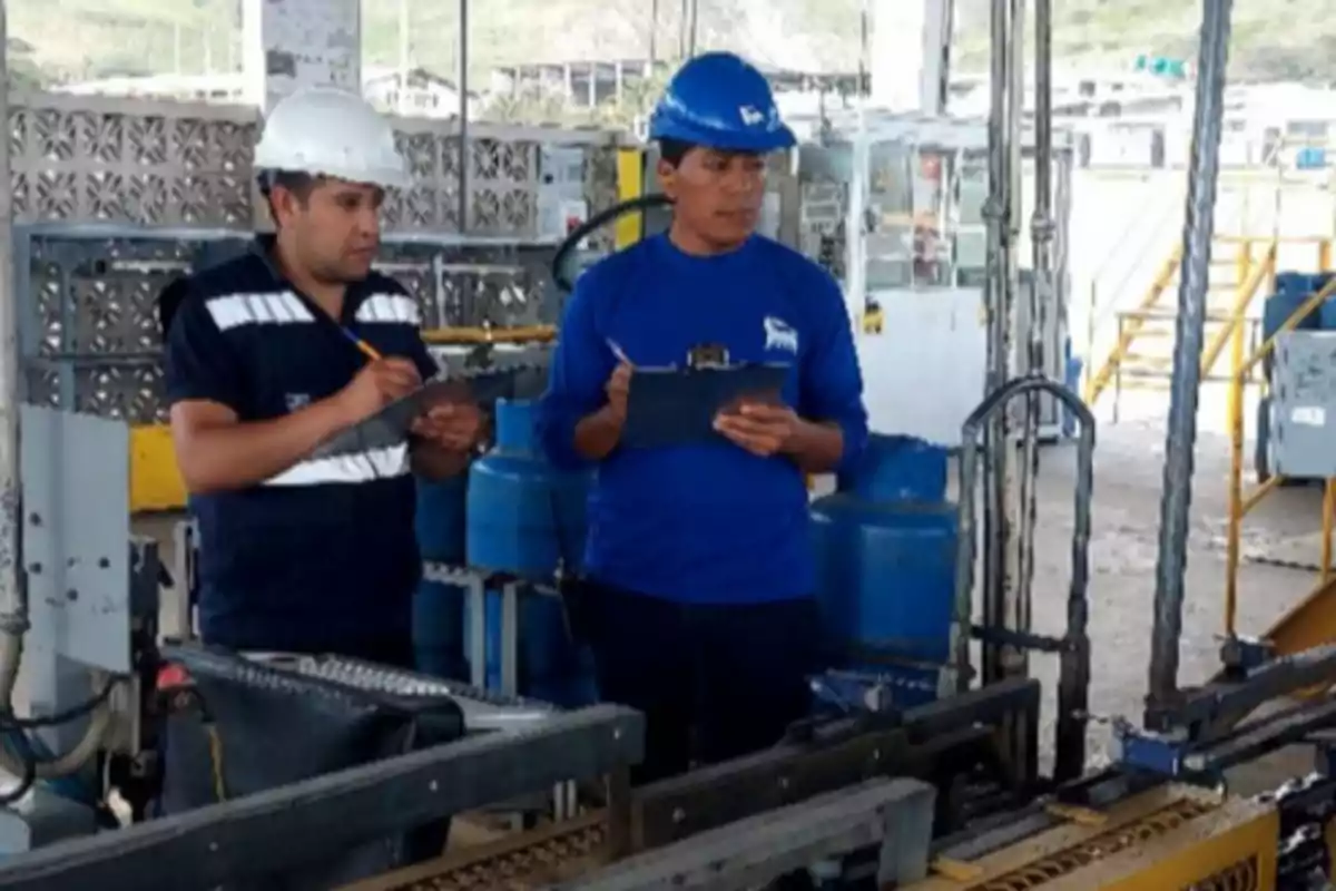 Two workers with safety helmets review documents in an industrial plant.