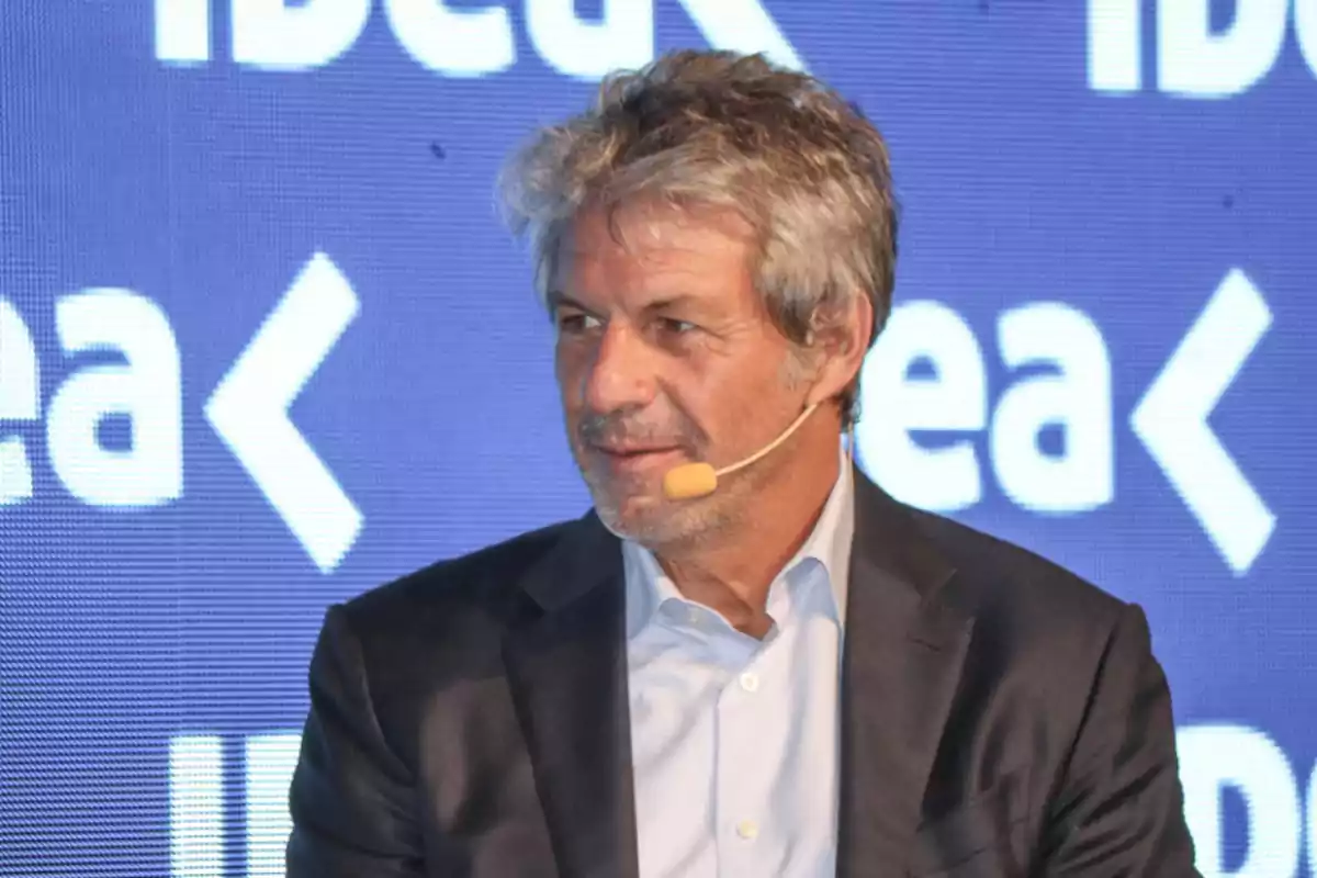 A man in a suit with a microphone at an event with a blue background that has the word A man in a suit with a microphone at an event with a blue background that has the word