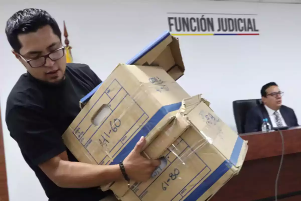 A man carries several cardboard boxes in a room with a sign that says A man carries several cardboard boxes in a room with a sign that says