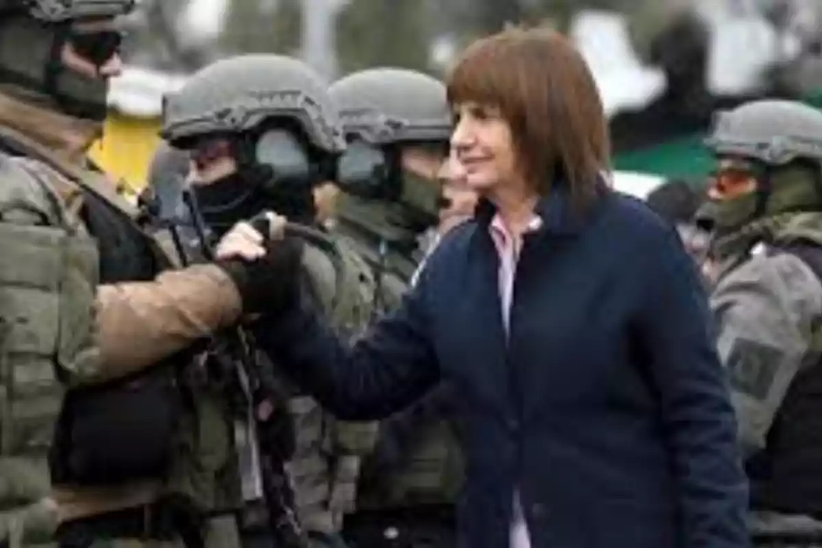 Una mujer saluda a un grupo de personas vestidas con uniformes tácticos y cascos en un entorno exterior. Una mujer saluda a un grupo de personas vestidas con uniformes tácticos y cascos en un entorno exterior.