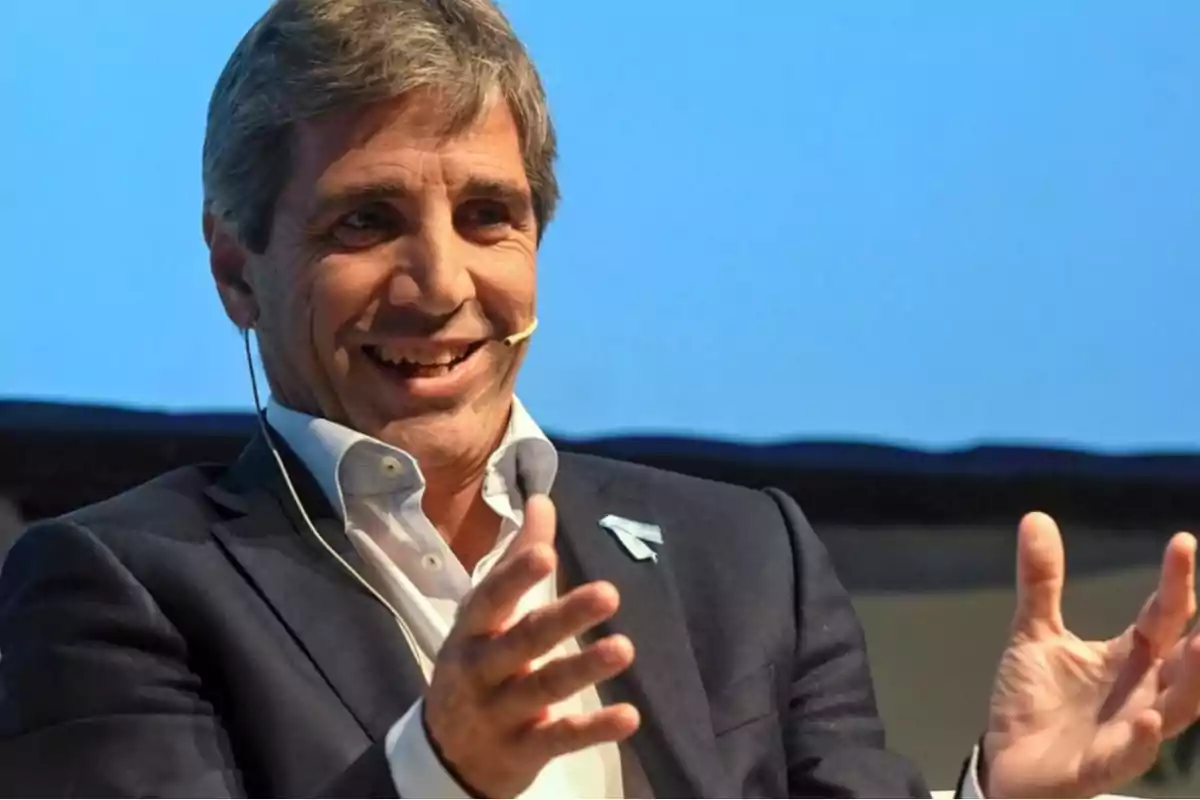 Hombre de cabello canoso con traje oscuro y camisa clara sonriendo mientras habla con un micrófono de diadema