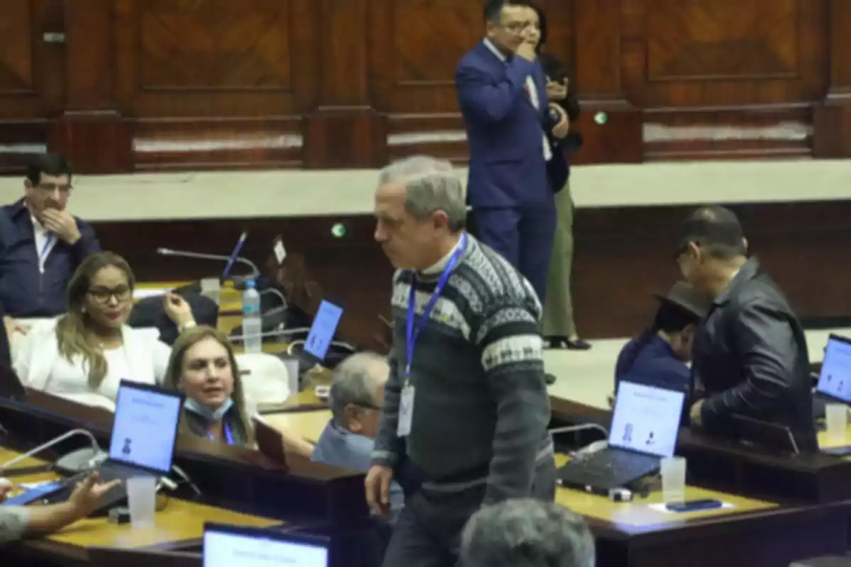 People gathered in a legislative chamber with laptops and documents on the tables