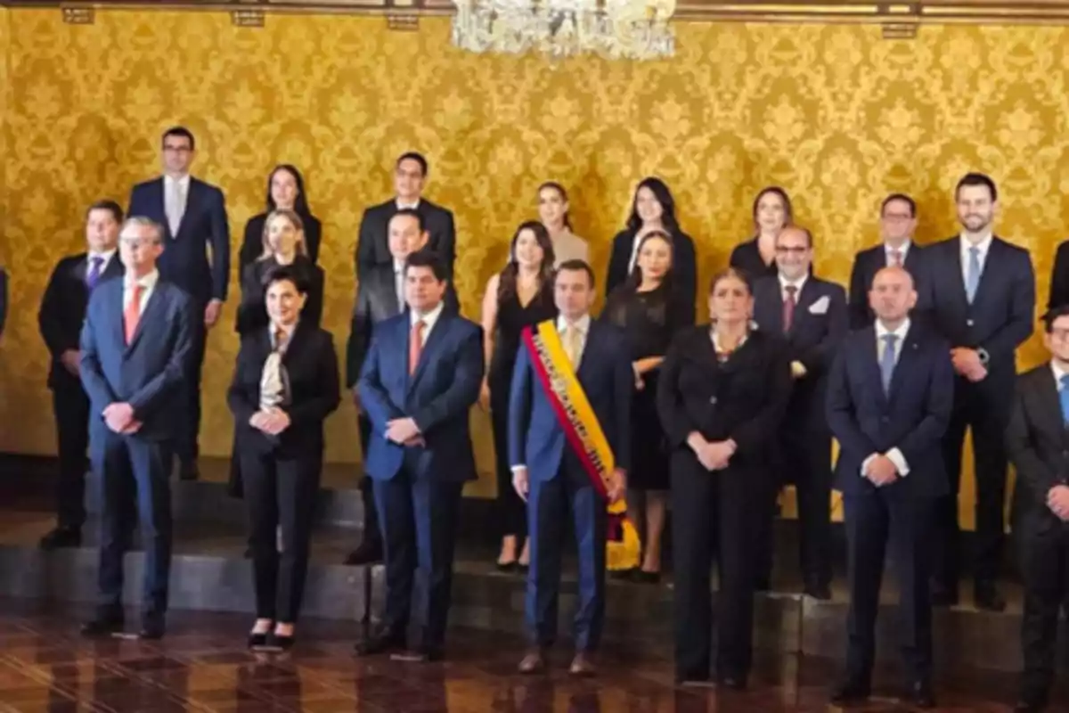 Group of people dressed formally posing in an elegant room with golden walls and a chandelier, one person in the center wearing a presidential sash. Group of people dressed formally posing in an elegant room with golden walls and a chandelier, one person in the center wearing a presidential sash.