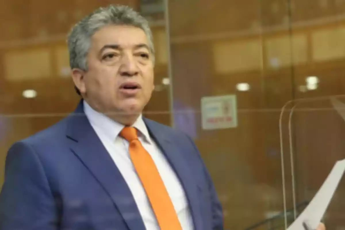 Gray-haired man in a blue suit and orange tie holding some papers in an office setting Gray-haired man in a blue suit and orange tie holding some papers in an office setting