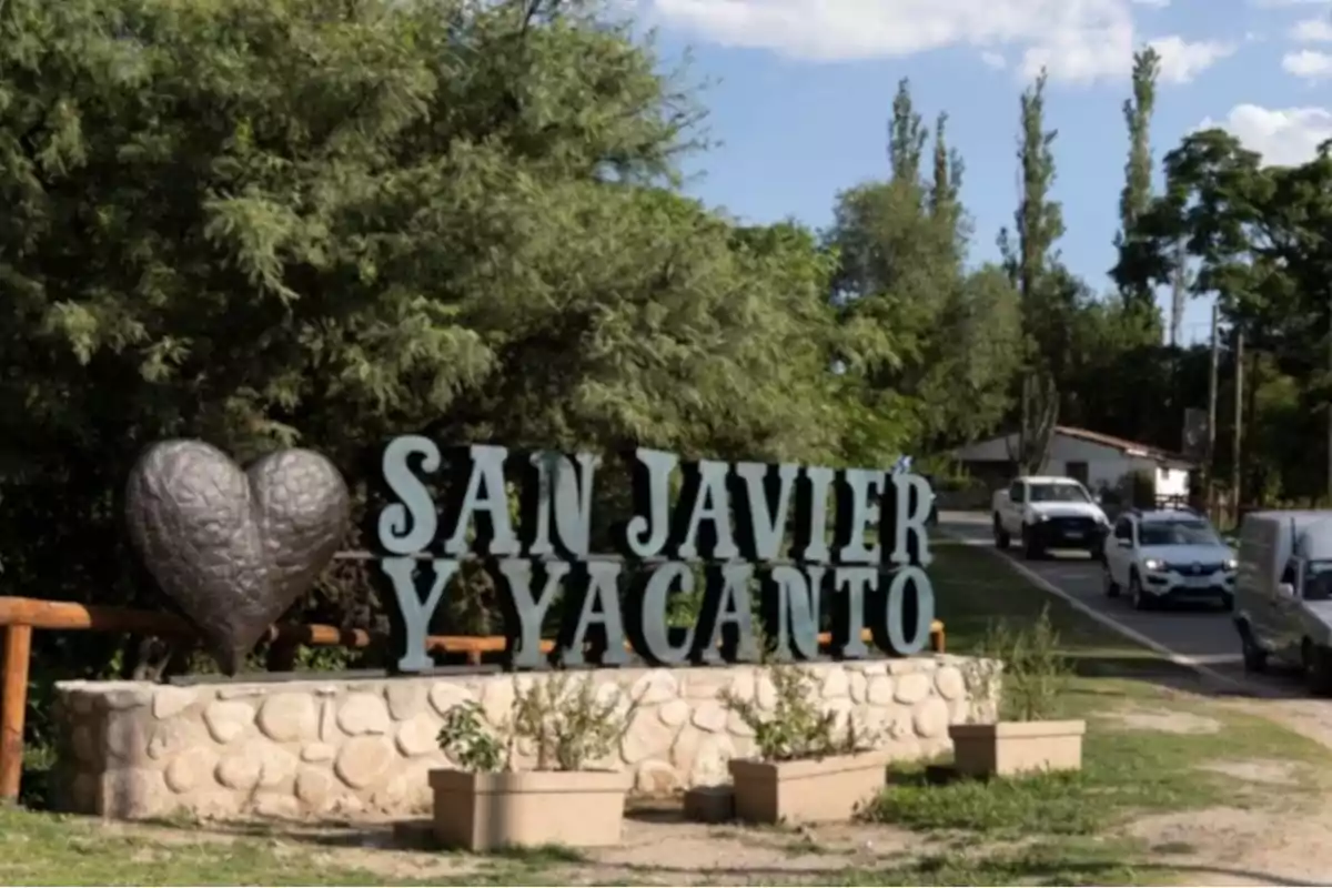 Welcome sign to San Javier and Yacanto next to a heart sculpture surrounded by vegetation and cars driving on a nearby street