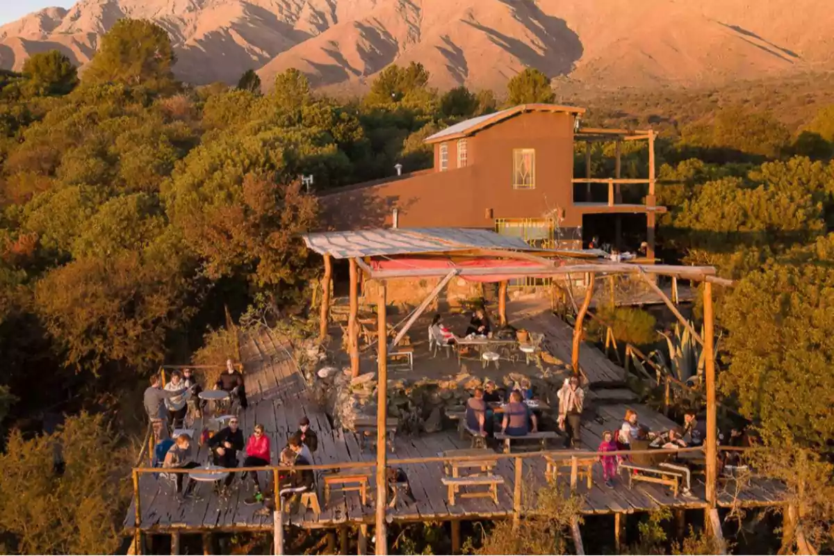 People sitting on a wooden terrace surrounded by trees and mountains at sunset People sitting on a wooden terrace surrounded by trees and mountains at sunset