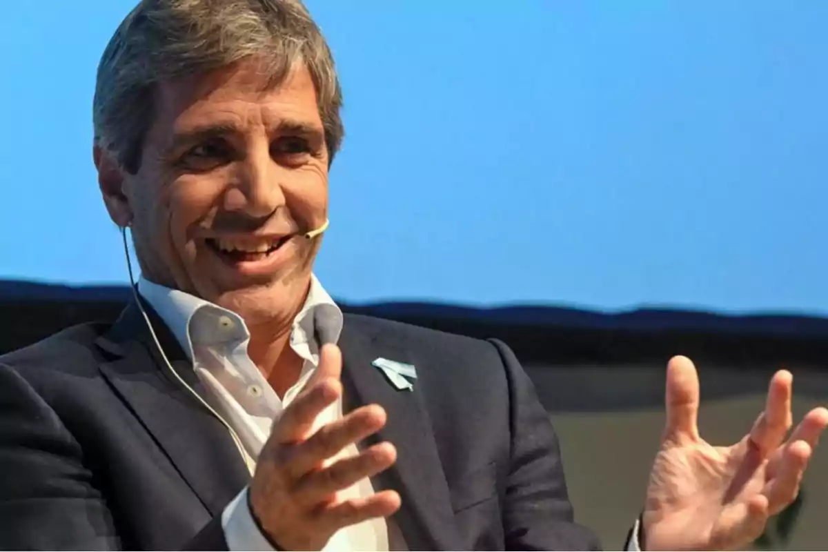 Gray-haired man in a dark suit smiling while speaking with a headset microphone and a blue background Gray-haired man in a dark suit smiling while speaking with a headset microphone and a blue background