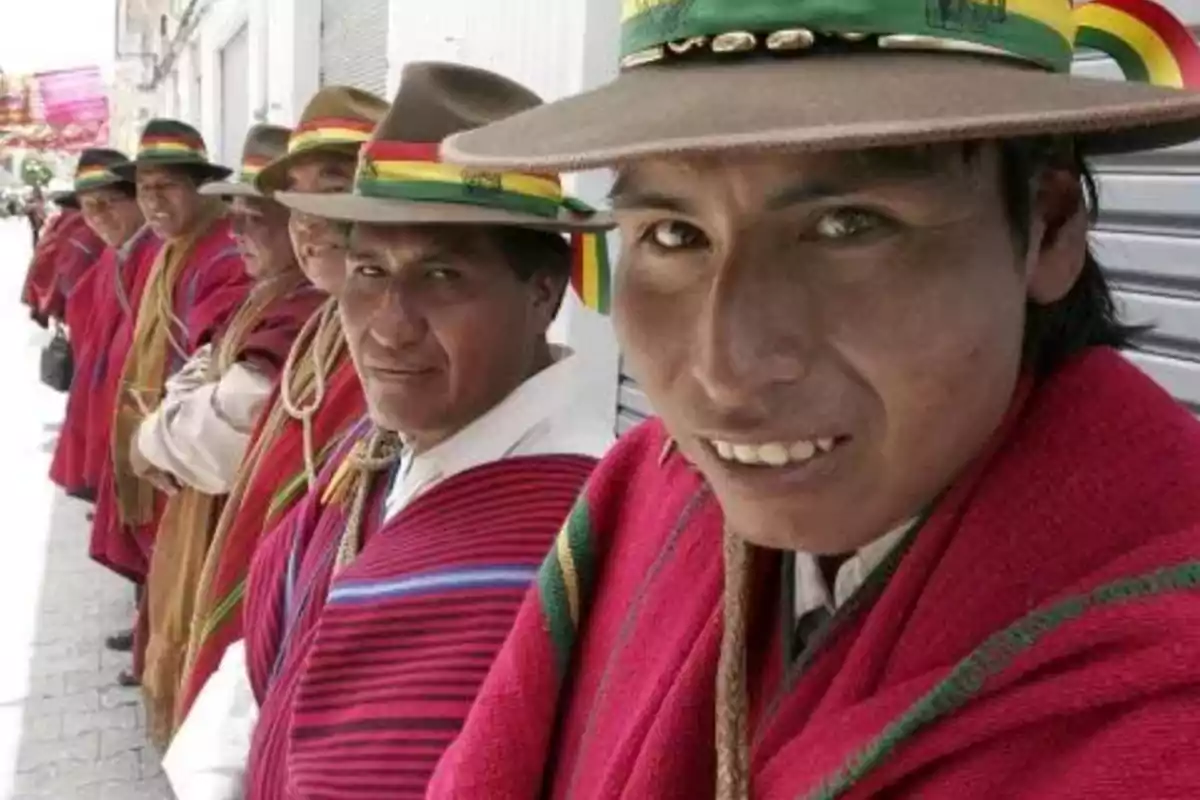 Group of men wearing red ponchos and traditional hats with colorful ribbons, lined up on a street