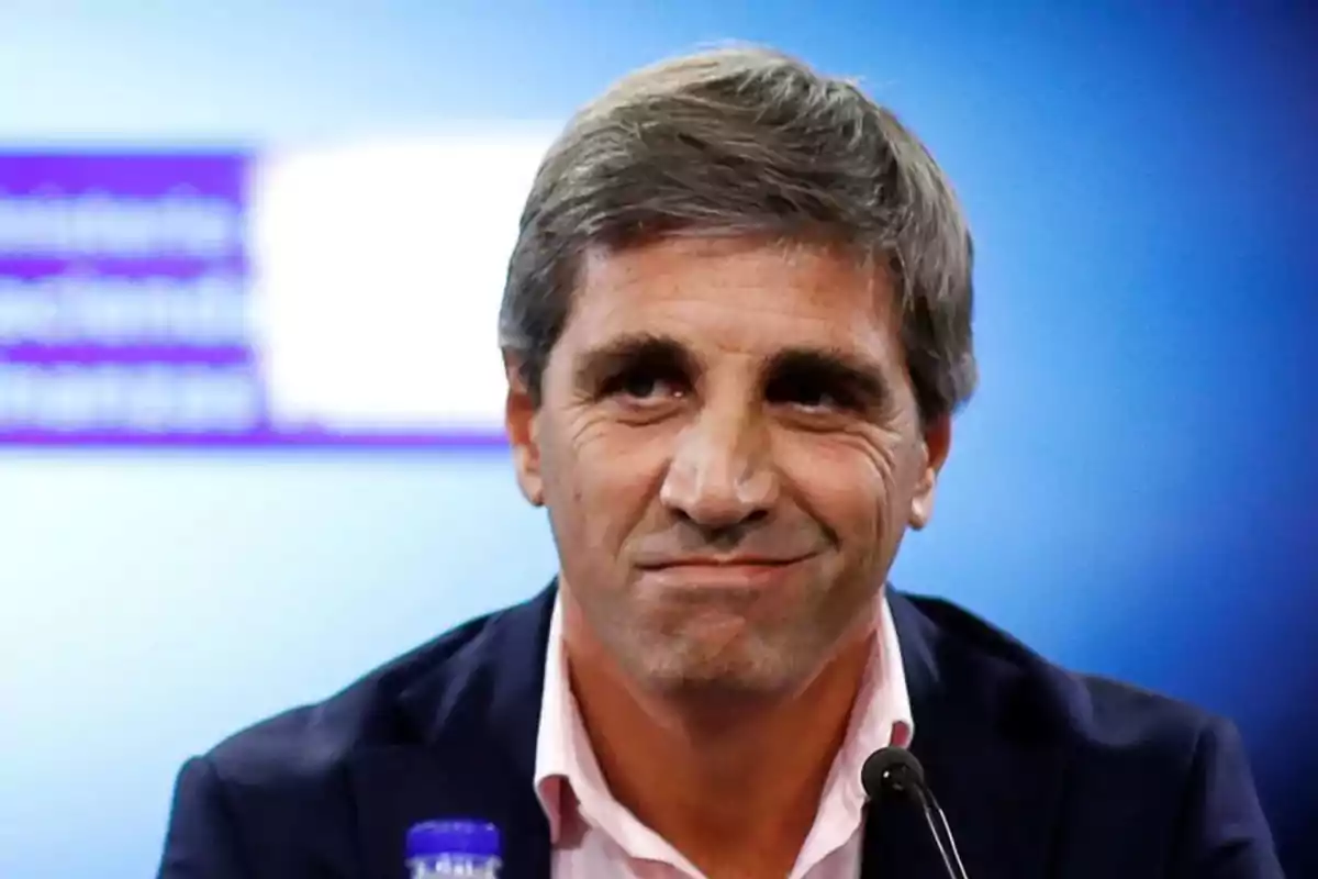 Hombre de cabello canoso y corto con expresión seria usando saco oscuro y camisa clara frente a un fondo azul