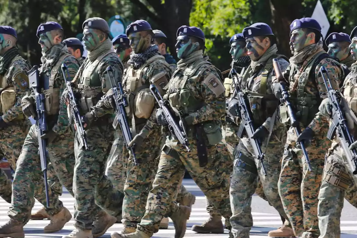 Soldados con uniforme de camuflaje y la cara pintada marchan en formación llevando rifles Soldados con uniforme de camuflaje y la cara pintada marchan en formación llevando rifles