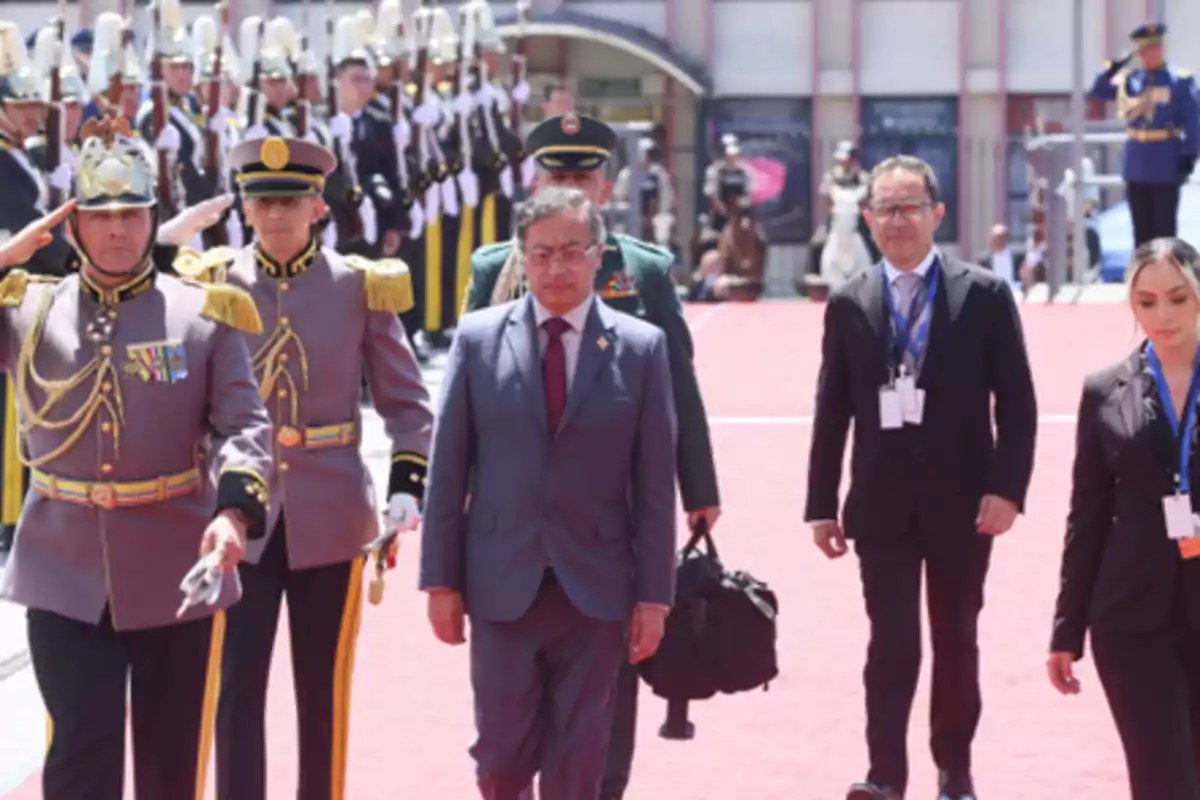 Un grupo de personas camina por una alfombra roja durante una ceremonia oficial con guardias uniformados al fondo
