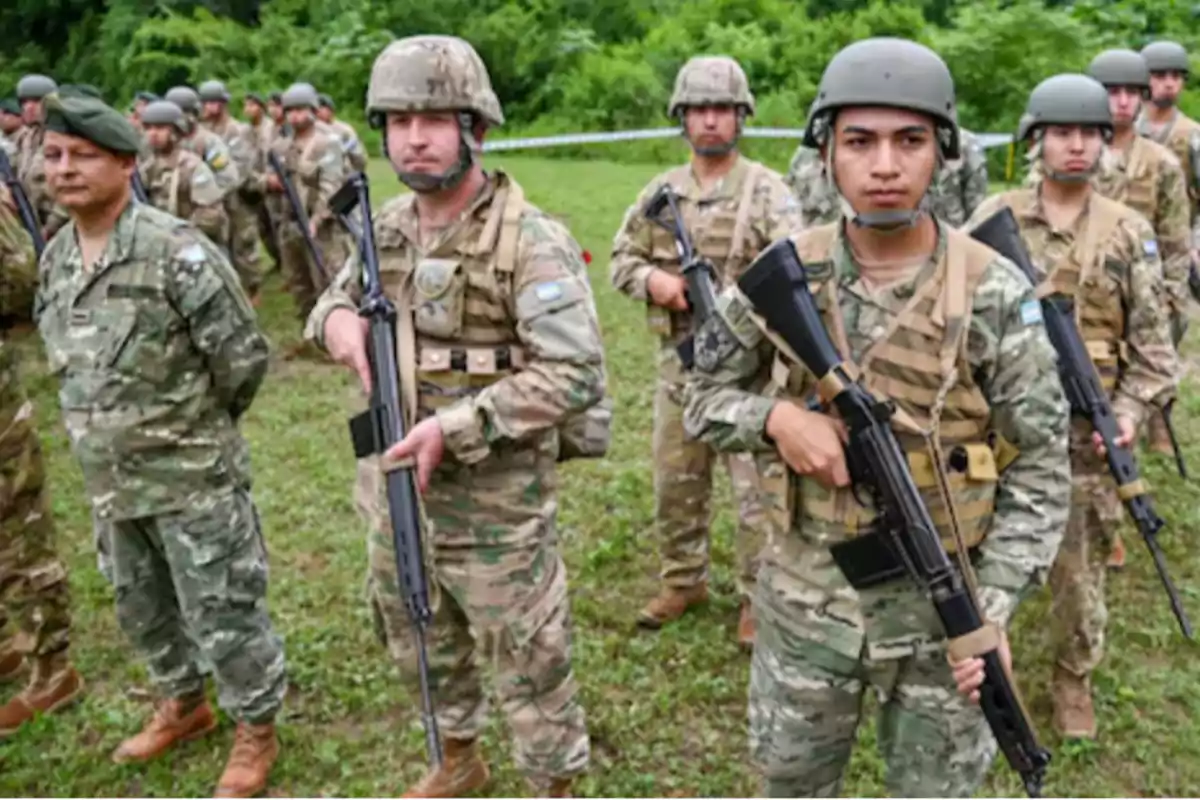 Soldados con uniforme de camuflaje y cascos en formación sobre césped sosteniendo rifles en un entorno al aire libre con vegetación al fondo Soldados con uniforme de camuflaje y cascos en formación sobre césped sosteniendo rifles en un entorno al aire libre con vegetación al fondo