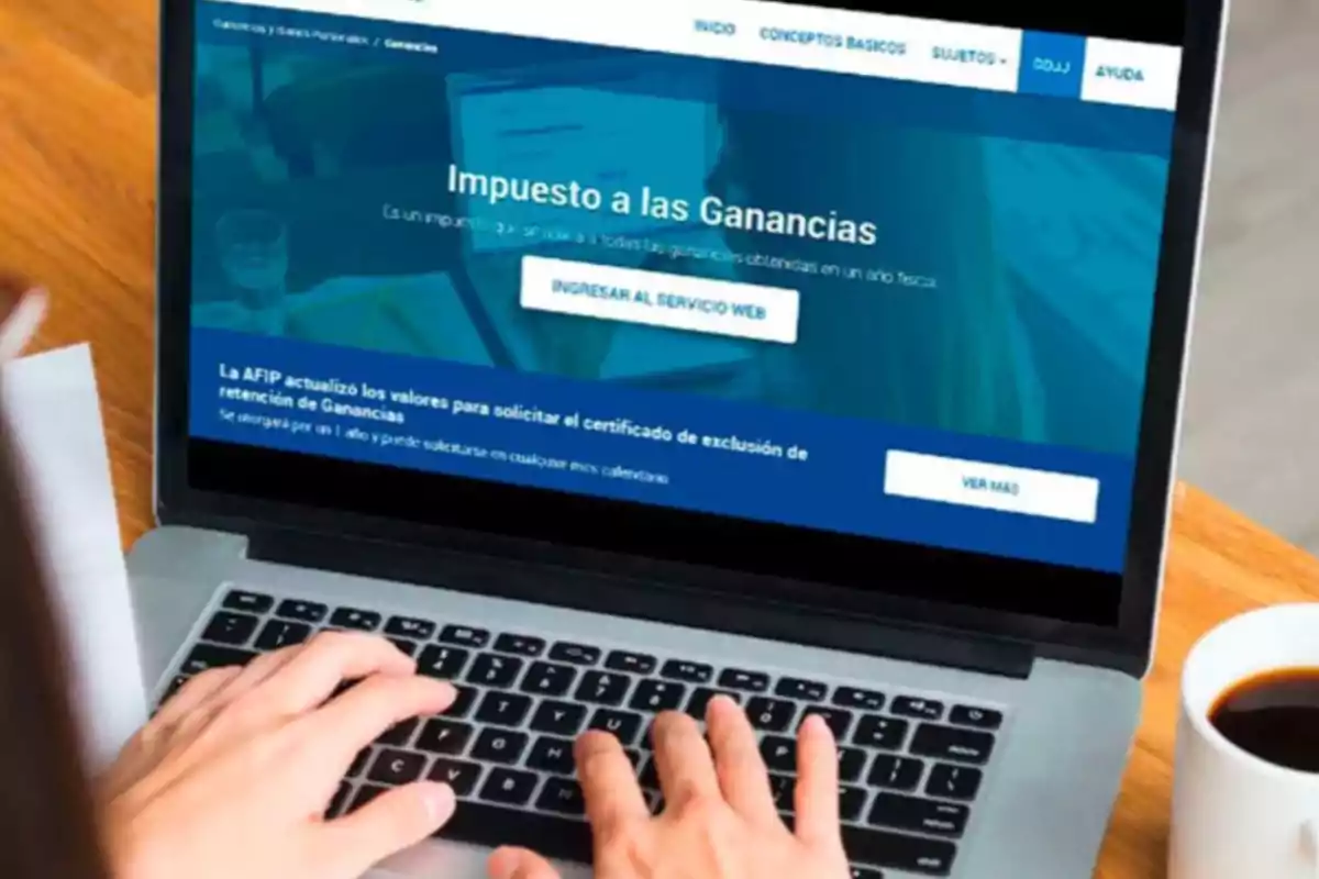 Persona usando una laptop para consultar información sobre el impuesto a las ganancias en la página web de la AFIP con una taza de café al lado