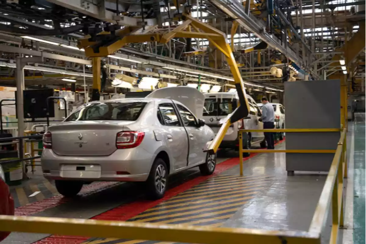 Automobile assembly line in a factory with several silver cars and a worker inspecting one of them Automobile assembly line in a factory with several silver cars and a worker inspecting one of them