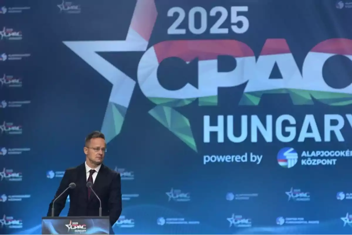 A man in a dark suit and tie speaks at a podium during a CPAC 2025 event in Hungary, with a large backdrop displaying the name of the event. A man in a dark suit and tie speaks at a podium during a CPAC 2025 event in Hungary, with a large backdrop displaying the name of the event.