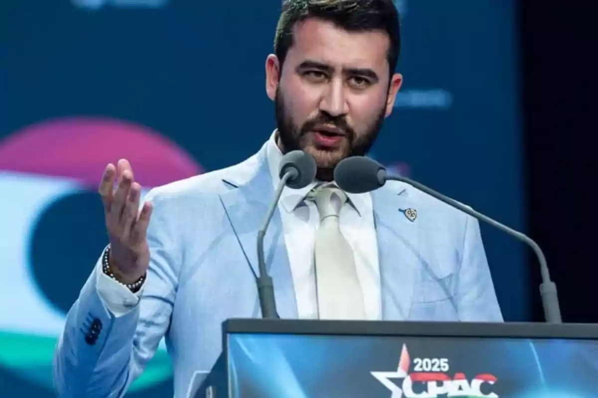 Man with a beard and light blue jacket speaking at a podium with two microphones at a CPAC 2025 event Man with a beard and light blue jacket speaking at a podium with two microphones at a CPAC 2025 event