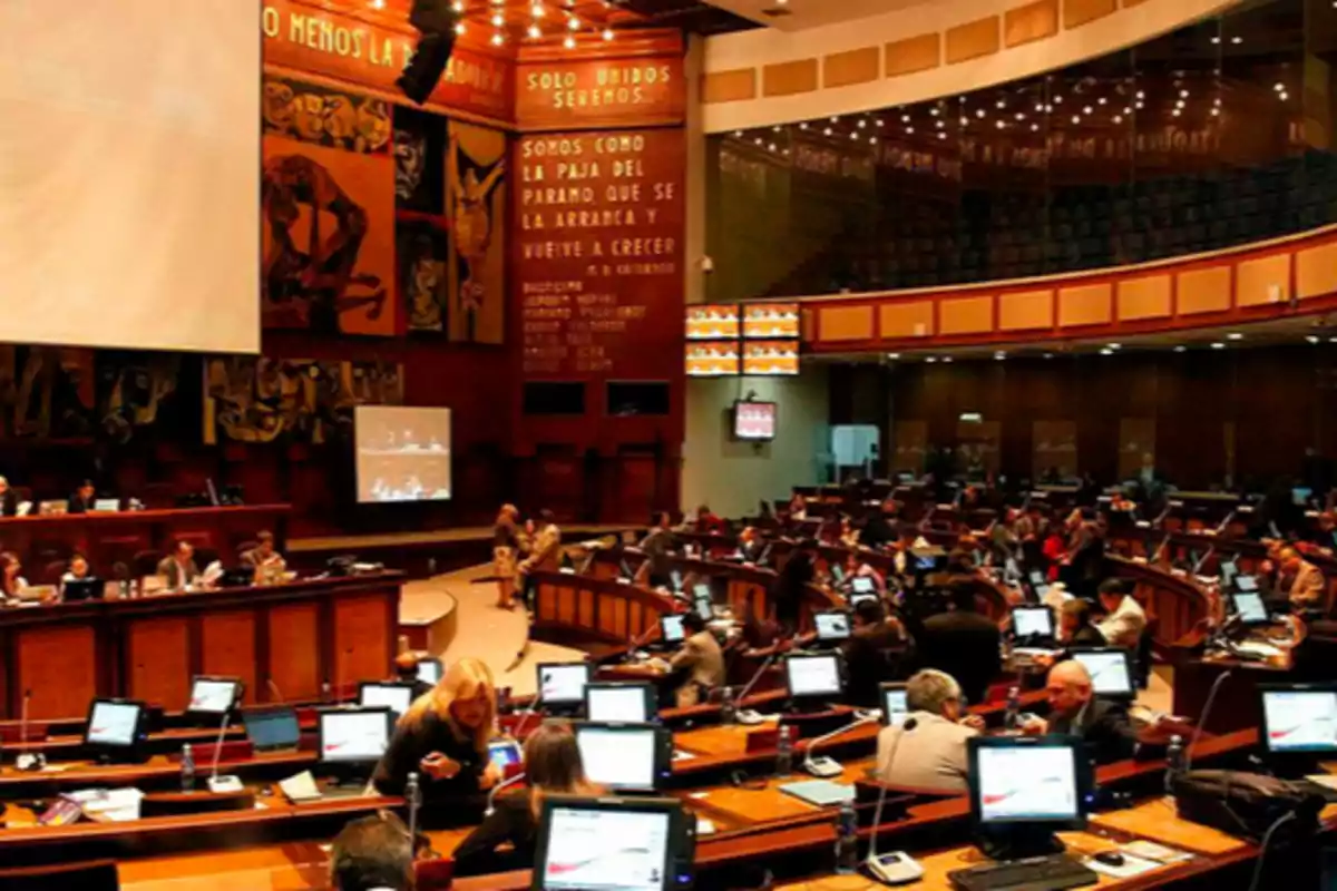 People working and talking in a parliamentary chamber with computers and screens on at their desks