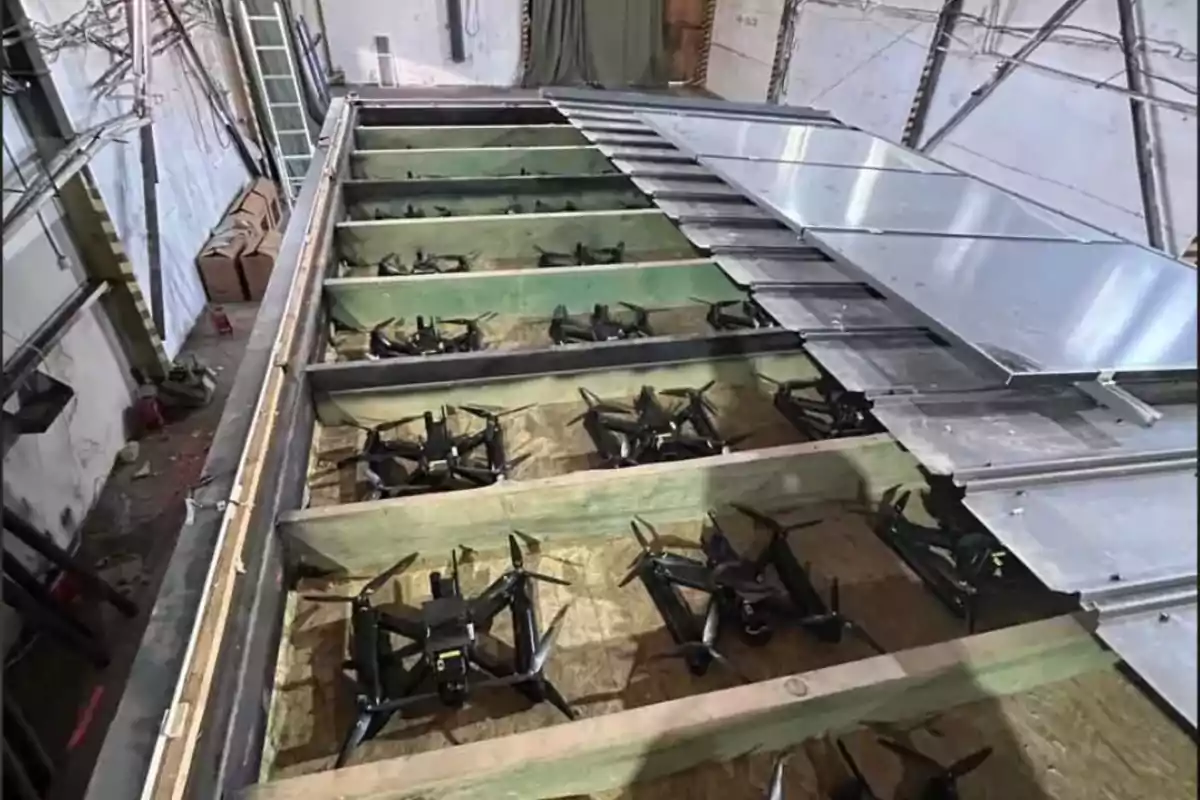 Varios drones están almacenados en compartimentos de madera bajo una estructura metálica dentro de un edificio industrial. Varios drones están almacenados en compartimentos de madera bajo una estructura metálica dentro de un edificio industrial.