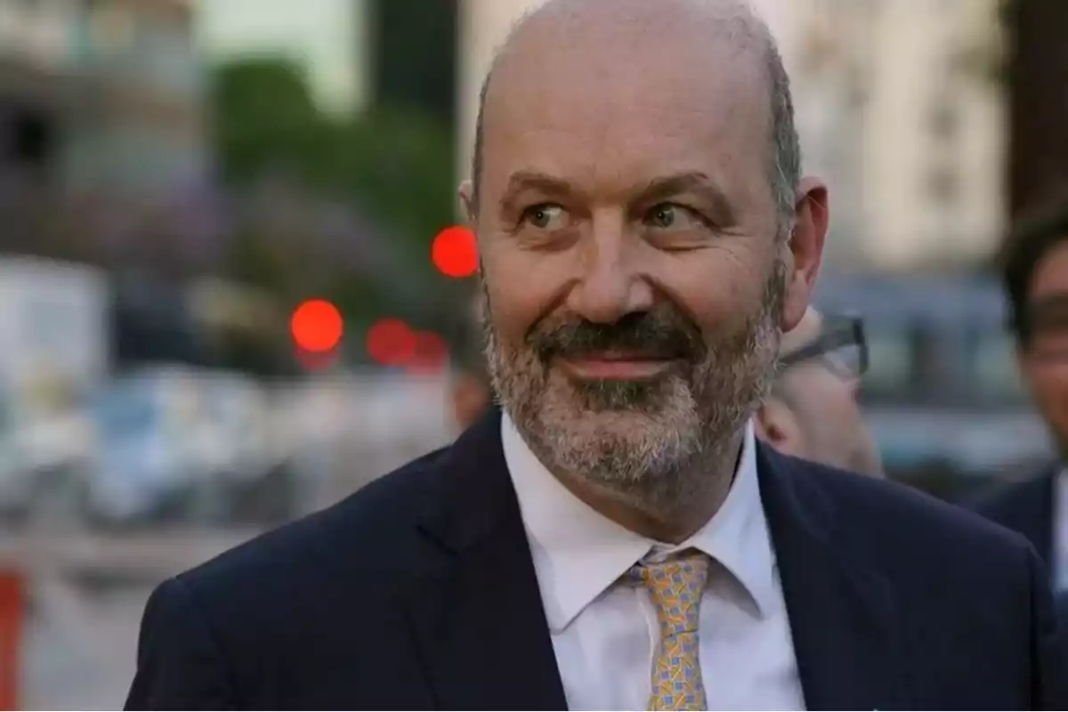Hombre calvo con barba y traje sonríe mientras está al aire libre en una ciudad con luces desenfocadas de fondo