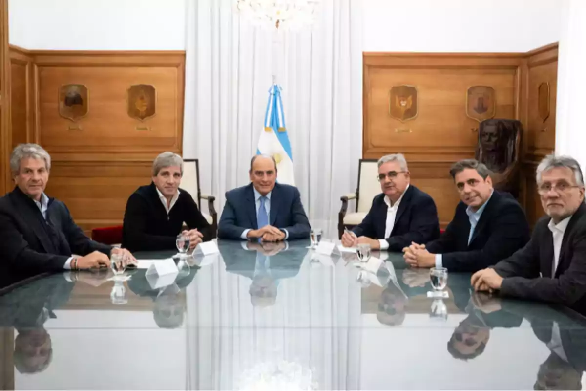 Six men sitting around a glass table in a formal room with wooden walls and an Argentine flag in the background