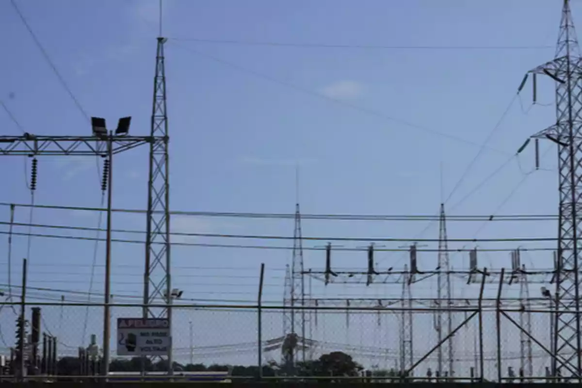 Fenced electrical substation with high-voltage towers and cables under a clear sky Fenced electrical substation with high-voltage towers and cables under a clear sky