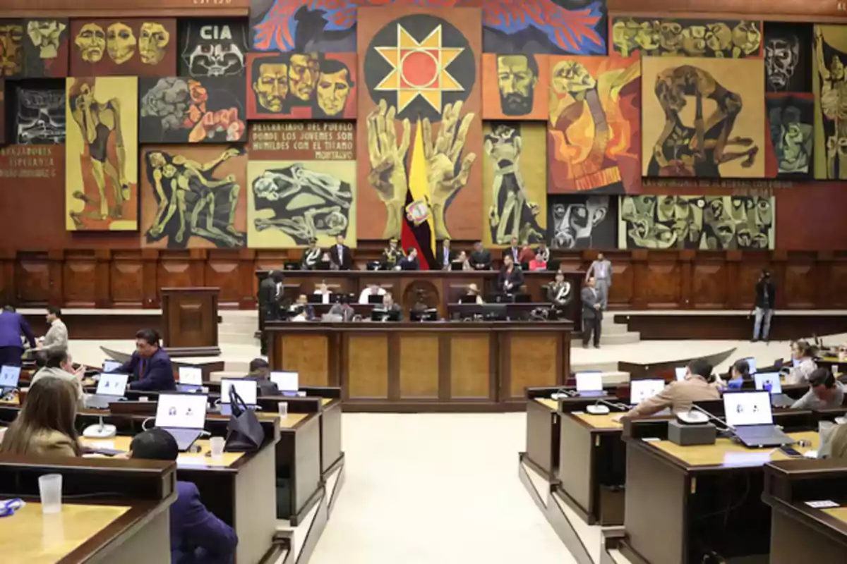 People working in a parliamentary chamber with colorful murals and a national flag in the center People working in a parliamentary chamber with colorful murals and a national flag in the center