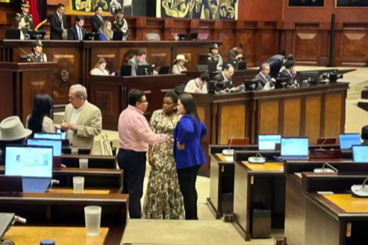 People talking and working inside a parliamentary chamber with laptops on the desks People talking and working inside a parliamentary chamber with laptops on the desks