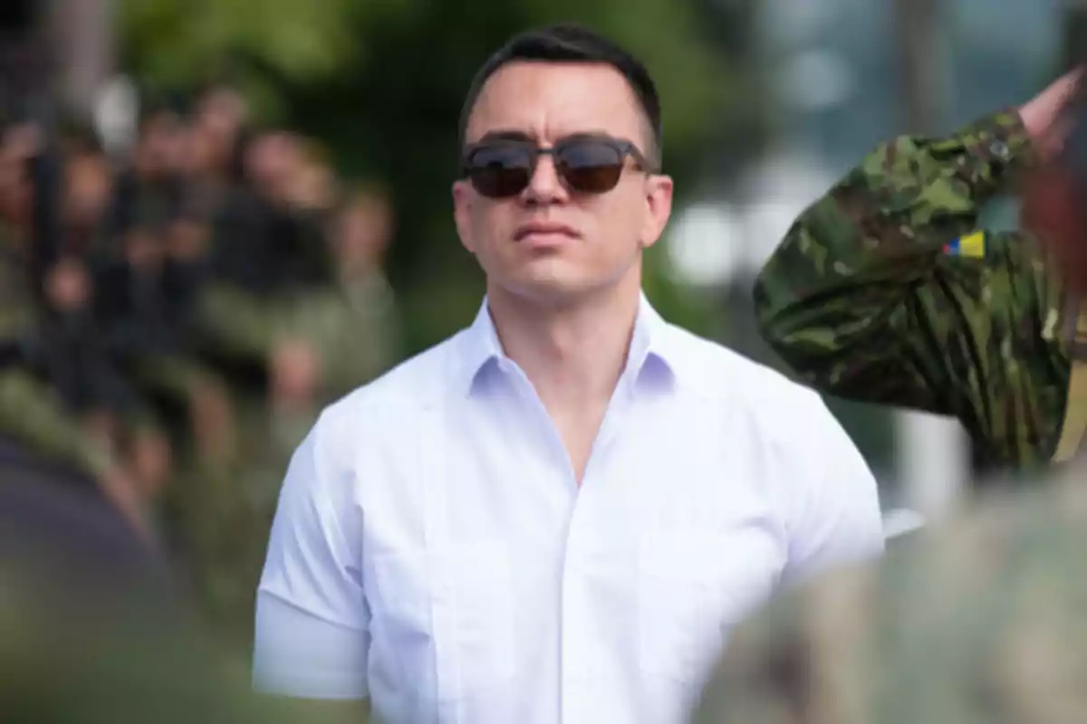 Man wearing sunglasses and a short-sleeved white jersey surrounded by people in military uniforms in an outdoor setting