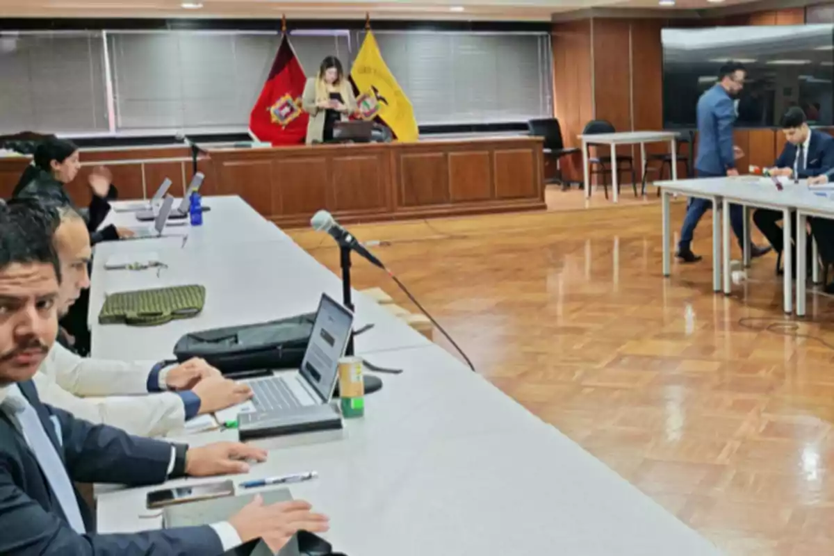 People sitting in a meeting room with laptops on the table and official flags in the background