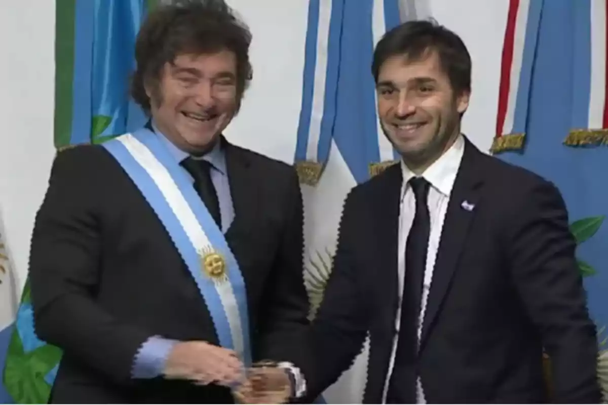 Dos hombres de traje sonríen y se dan la mano frente a banderas argentinas Dos hombres de traje sonríen y se dan la mano frente a banderas argentinas