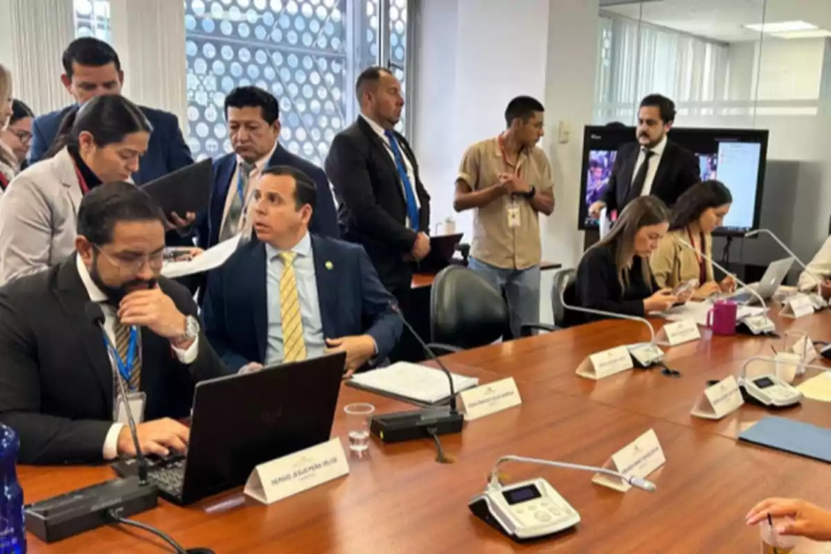 Several people gathered in a conference room working with laptops and documents on a long table.