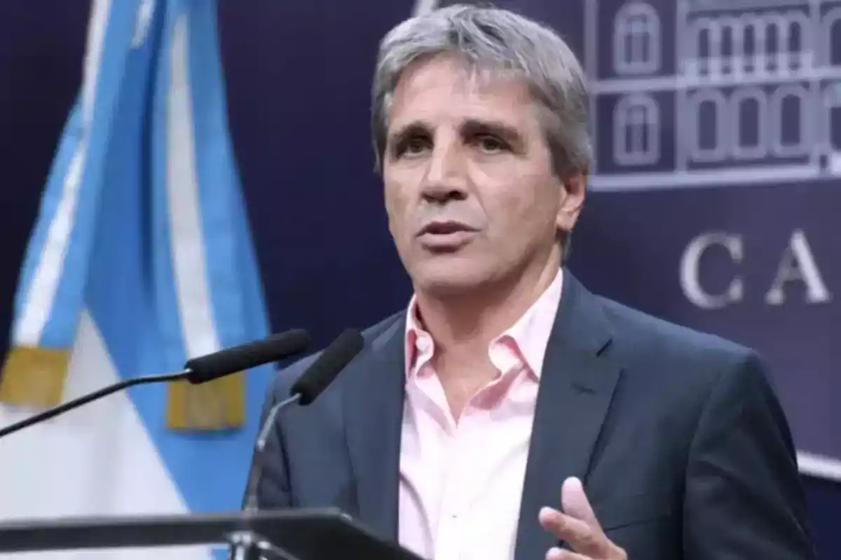Hombre de cabello canoso hablando frente a micrófonos con una bandera argentina de fondo