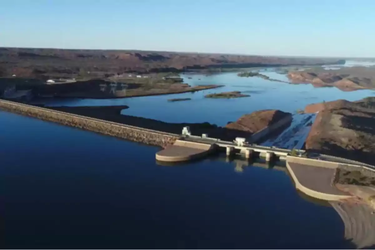 Vista aérea de una represa hidroeléctrica rodeada de agua y colinas áridas bajo un cielo despejado Vista aérea de una represa hidroeléctrica rodeada de agua y colinas áridas bajo un cielo despejado