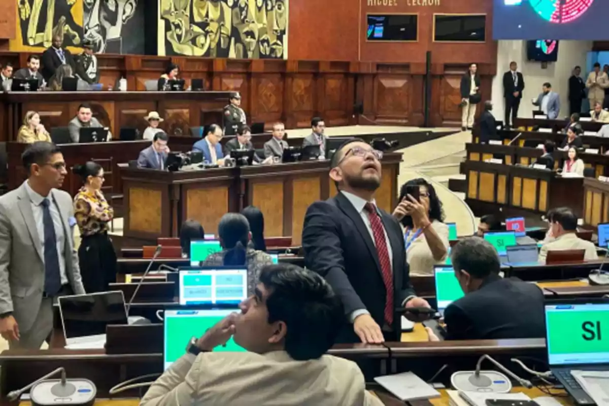 People in a legislative chamber during a parliamentary session, with computers displaying voting results and a formal working environment. People in a legislative chamber during a parliamentary session, with computers displaying voting results and a formal working environment.