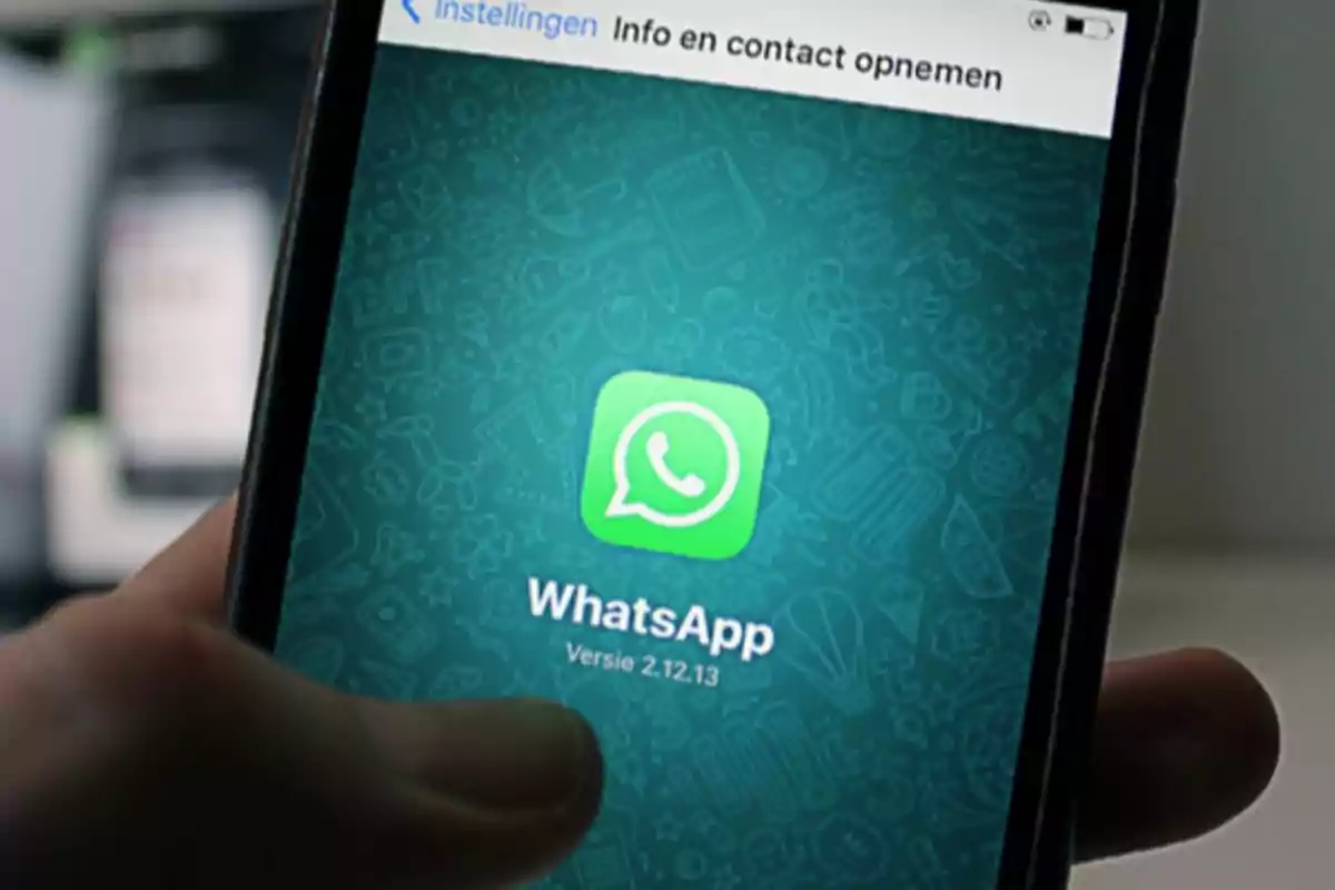 Persona sosteniendo un teléfono móvil que muestra la pantalla de inicio de la aplicación WhatsApp