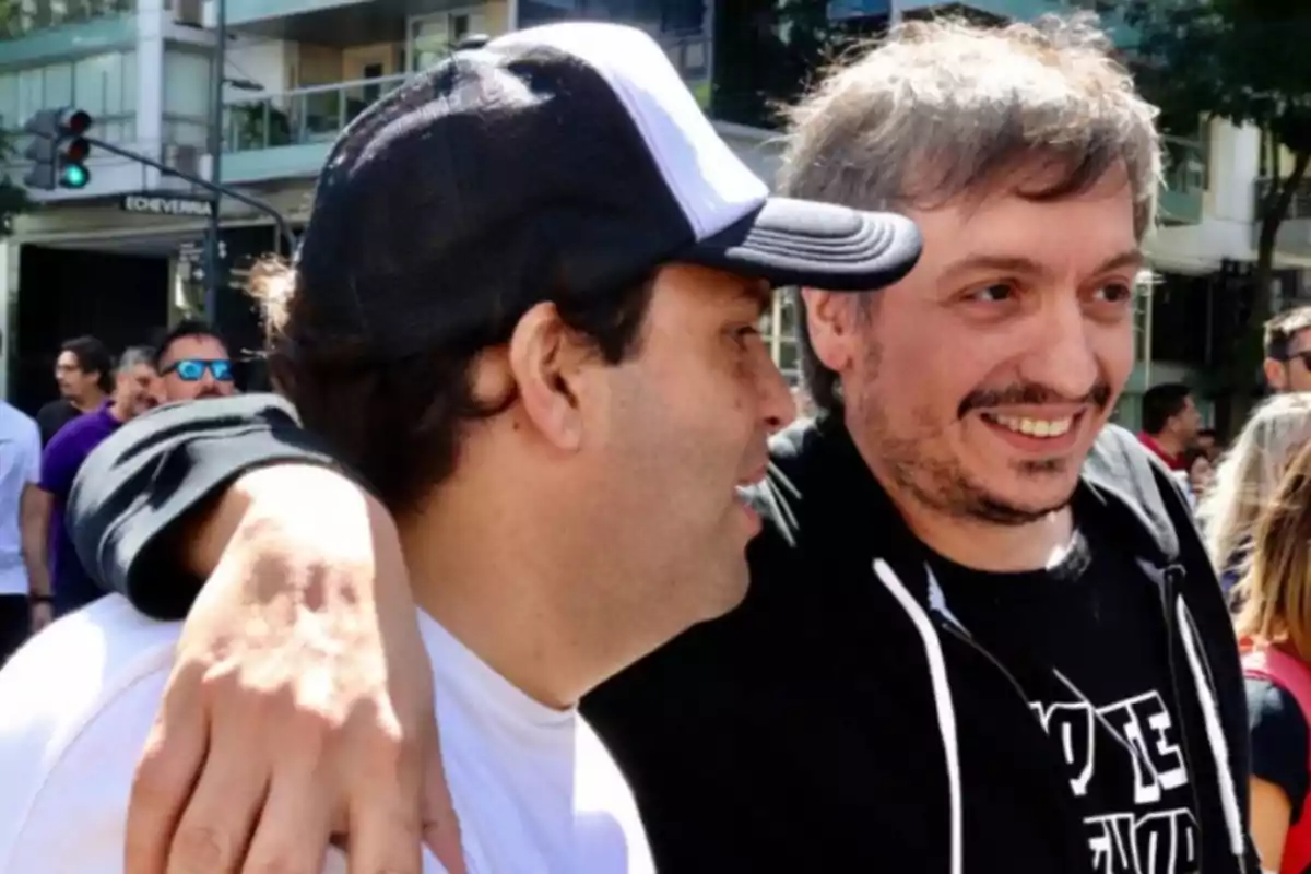Two men smile and hug on a busy street during the day.