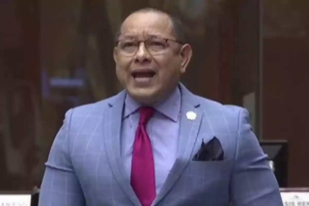 Middle-aged man with glasses and a light blue suit with a fuchsia tie speaking in a formal setting Middle-aged man with glasses and a light blue suit with a fuchsia tie speaking in a formal setting