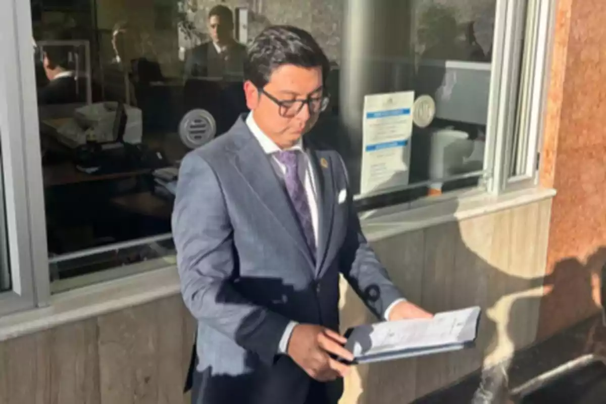 Man with glasses and a suit holding documents in front of an office window Man with glasses and a suit holding documents in front of an office window