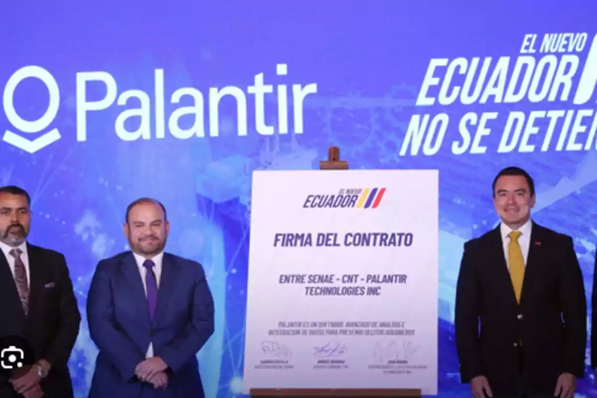 Three men in suits pose next to a contract signing sign between SENAE, CNT, and Palantir Technologies Inc, with a blue background displaying the Palantir logos and the slogan Three men in suits pose next to a contract signing sign between SENAE, CNT, and Palantir Technologies Inc, with a blue background displaying the Palantir logos and the slogan
