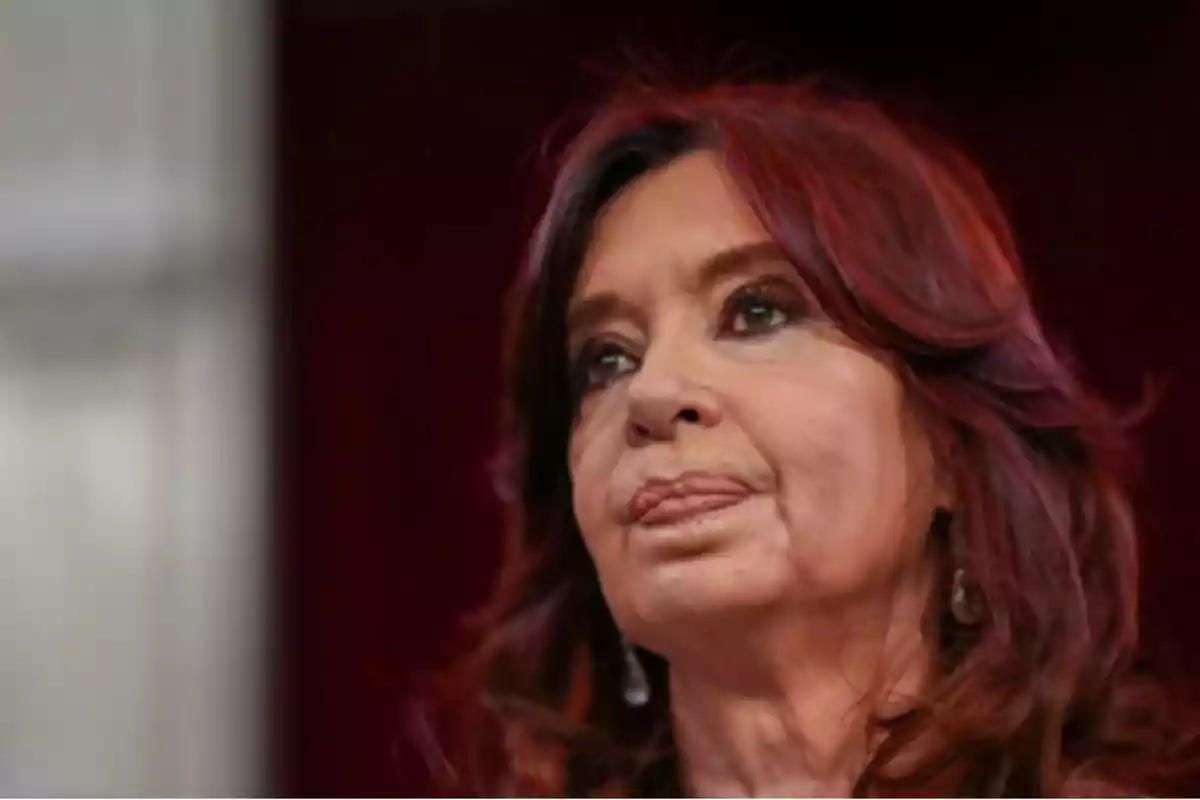 Mujer de cabello castaño rojizo y expresión seria mirando hacia el frente con fondo oscuro.