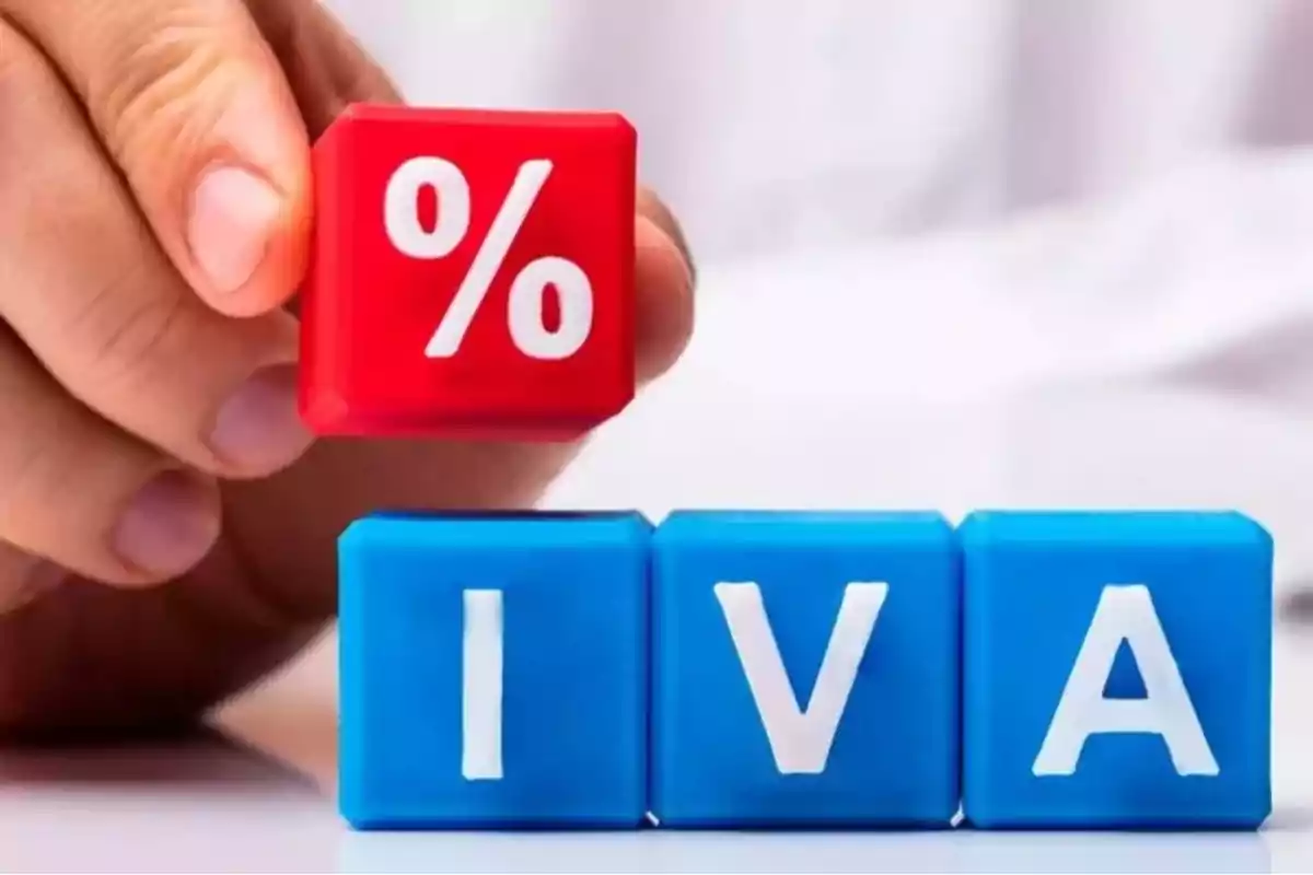 Mano sosteniendo un cubo rojo con el símbolo de porcentaje junto a tres cubos azules con las letras IVA