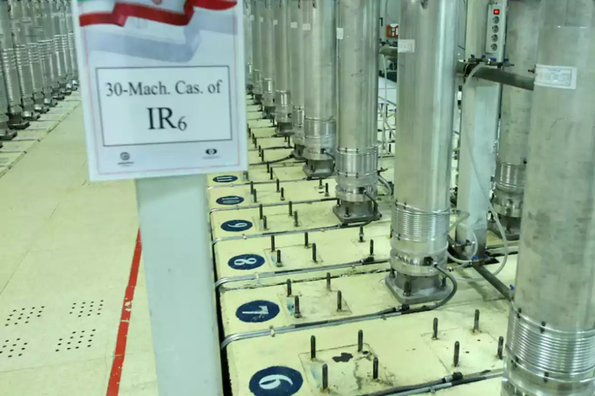Row of industrial metal centrifuges in a facility with a sign indicating IR6 and numbered bases on the floor Row of industrial metal centrifuges in a facility with a sign indicating IR6 and numbered bases on the floor