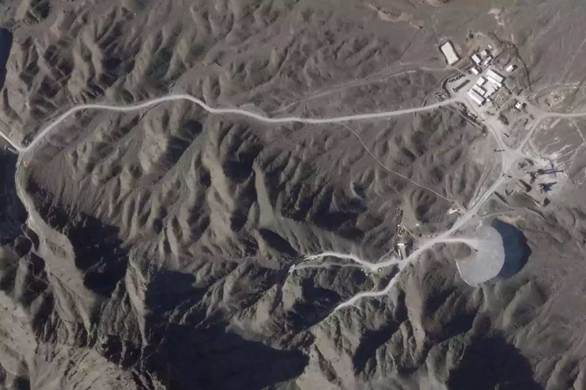 Aerial view of mountainous terrain with winding roads and a complex of buildings in the upper right. Aerial view of mountainous terrain with winding roads and a complex of buildings in the upper right.