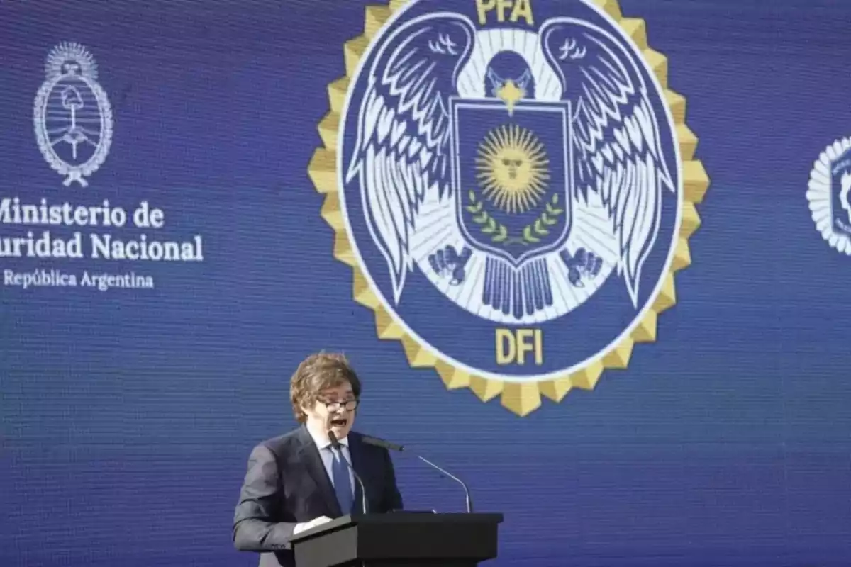 Un hombre con traje y corbata habla en un podio frente a un fondo azul con el escudo de la Policía Federal Argentina y el logo del Ministerio de Seguridad Nacional Un hombre con traje y corbata habla en un podio frente a un fondo azul con el escudo de la Policía Federal Argentina y el logo del Ministerio de Seguridad Nacional