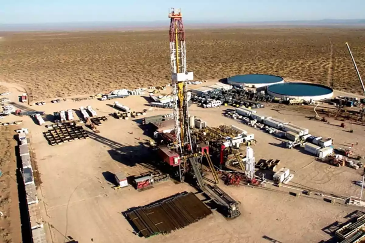 Plataforma de perforación petrolera en medio del desierto rodeada de maquinaria, vehículos y dos grandes tanques circulares de agua