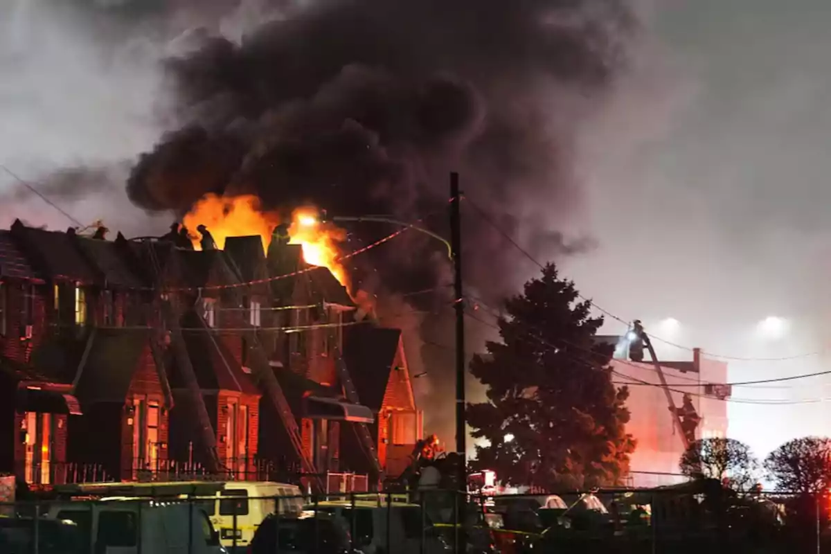 Incendio en un edificio residencial con bomberos trabajando para controlar las llamas y humo denso en el cielo.