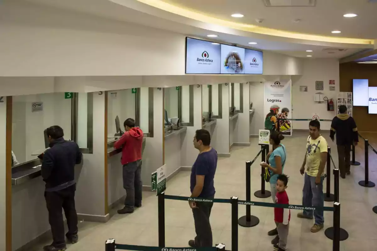 Personas haciendo fila en una sucursal bancaria con varios mostradores de atención.