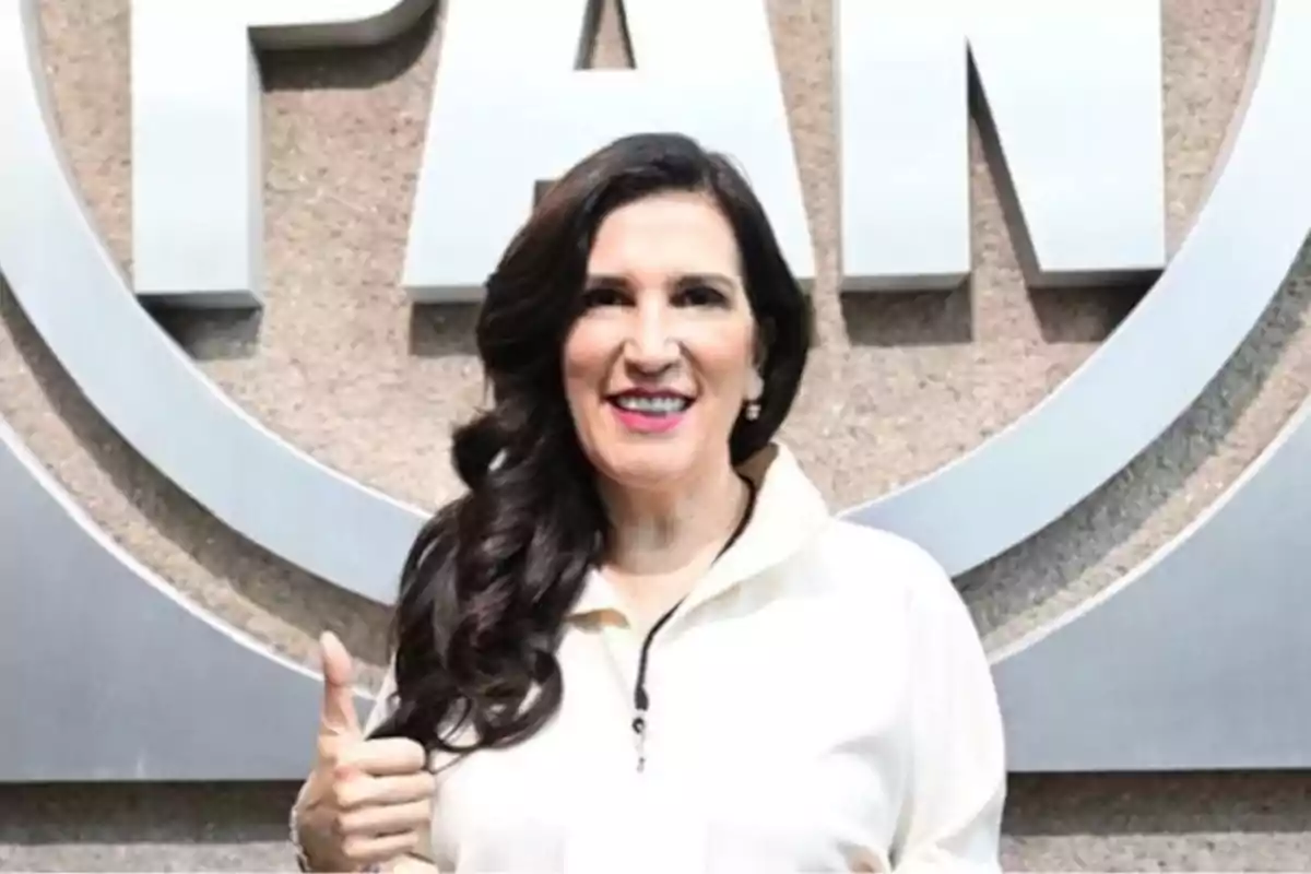 Woman smiling with a thumbs up in front of a logo on the wall.