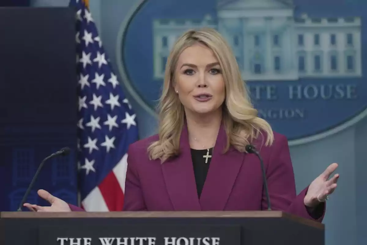 Una mujer hablando en un podio con el emblema de la Casa Blanca y una bandera de Estados Unidos al fondo.