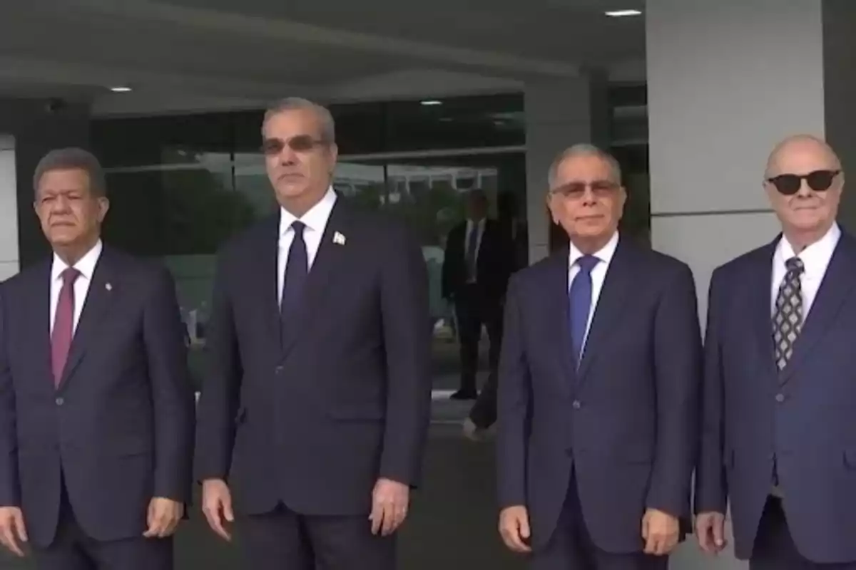Cuatro hombres vestidos con trajes formales posan juntos frente a un edificio moderno Cuatro hombres vestidos con trajes formales posan juntos frente a un edificio moderno